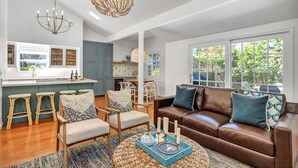 A spacious living room with a brown leather sofa, a dining area with a kitchen in the background, and large windows offering a view of greenery. - Your escape to Napa Valley (Yountville)