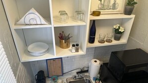 Et køkken med vask, hylder med vinglas, kaffemaskine og mikrobølgeovn.