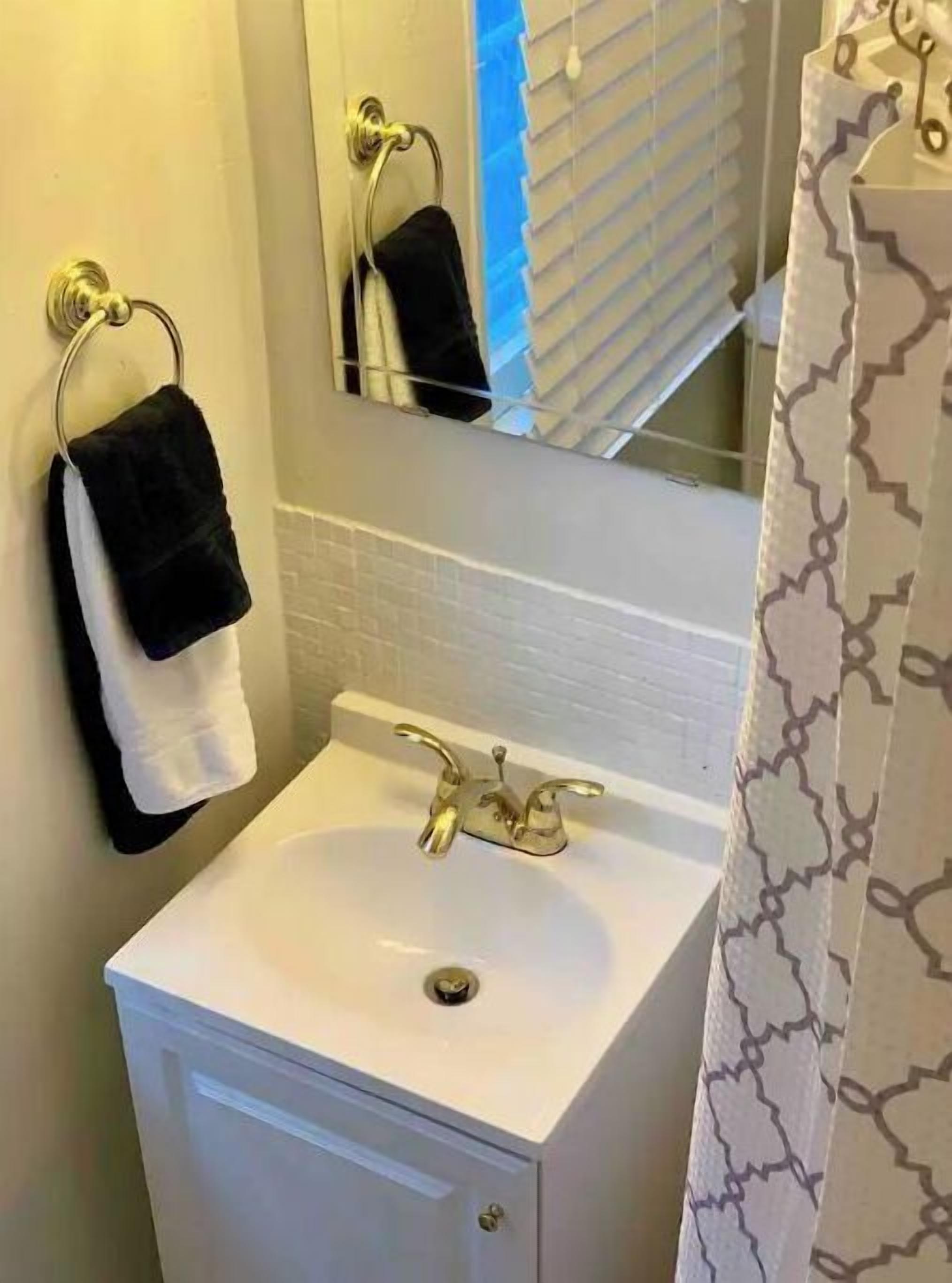 A bathroom with a white sink, a towel rack with two towels, a mirror, and a shower curtain with a geometric pattern.