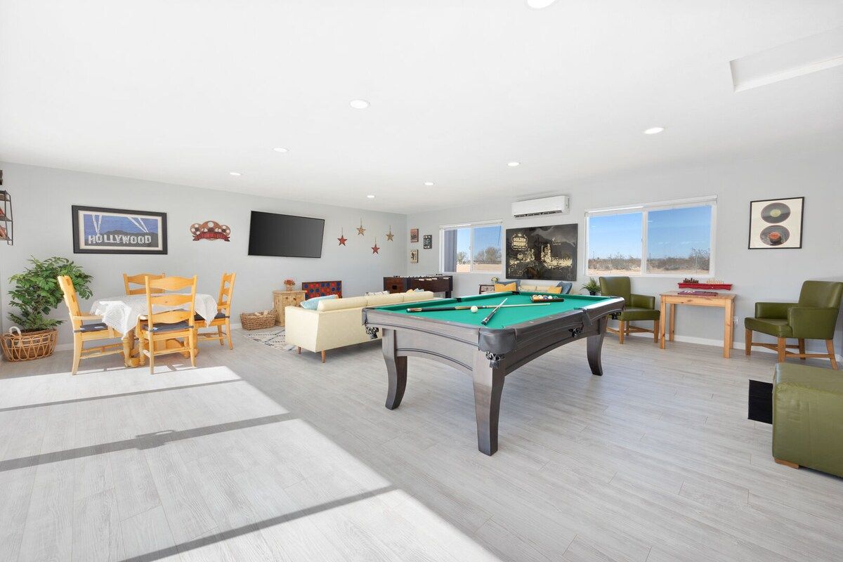 A modern living room with a pool table, comfortable seating, and a large window providing natural light.
