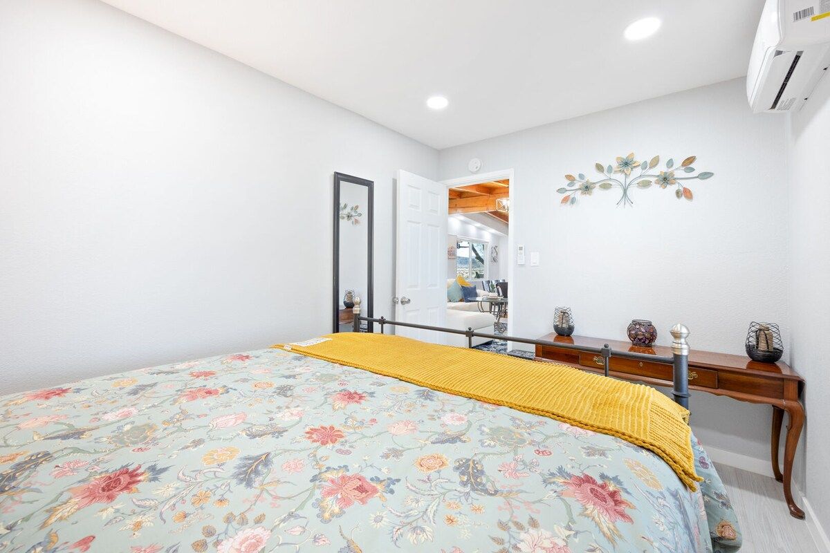 A bedroom with a bed, a wooden nightstand, a mirror, and a wall decoration.