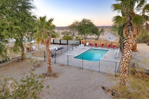 A swimming pool with lounge chairs and a fenced area, surrounded by trees and a desert landscape. - Mystic Views: Pool, Hot Tub, Game Room & Fire Pit! (Twentynine Palms)