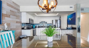 A modern kitchen with white cabinets, a central island with a glass top, and a hanging light fixture.