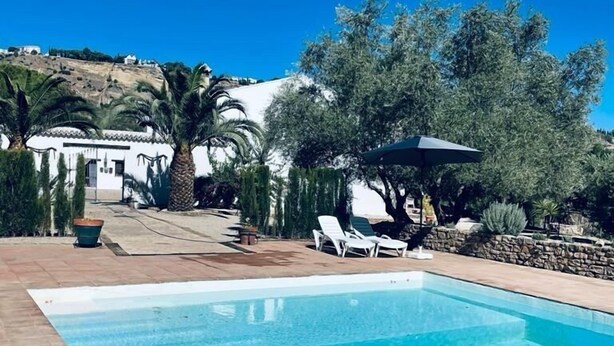 A swimming pool with a clear blue water, surrounded by a patio area with lounge chairs and a pergola. - Hotel La Mirada de Ronda  (Ronda)