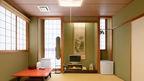 A traditional Japanese room with tatami flooring, a low table with a red mat, a television, a small refrigerator, and a sliding door leading to another room. - Business Ryokan Hotel Yukimiso (Toyama)