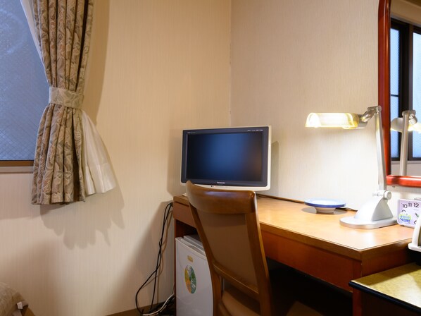 A hotel room with a desk, a computer monitor, a lamp, and a refrigerator.