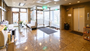 A reception area with a seating area, a reception desk, and a glass door entrance. - Business Ryokan Hotel Yukimiso (Toyama)