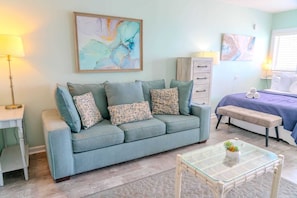 A living room with a sofa, a glass coffee table, and artwork on the walls.