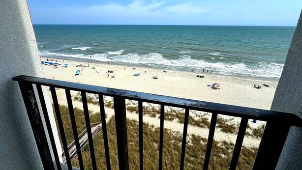 A beach view from a balcony with a railing, sandy beach, ocean, and a clear sky. - Palace 701 (Myrtle Beach)