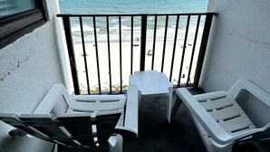 A balcony with two white plastic chairs and a small table, overlooking a beach with people in the distance. - Palace 701 (Myrtle Beach)