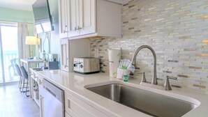 A kitchen with a stainless steel sink, white cabinets, a toaster, and a tiled backsplash. - Palace 701 (Myrtle Beach)