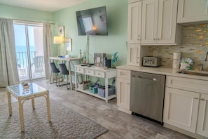 A kitchen with a dishwasher, a TV mounted on the wall, and a dining area with chairs and a table.