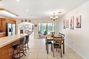 A spacious kitchen with a large island, wooden cabinets, and modern appliances. There is a dining area with a table and chairs, and a view of a backyard through large sliding glass doors. - Nice and quite neighborhood close to malls, parks and restaurants (Miami)