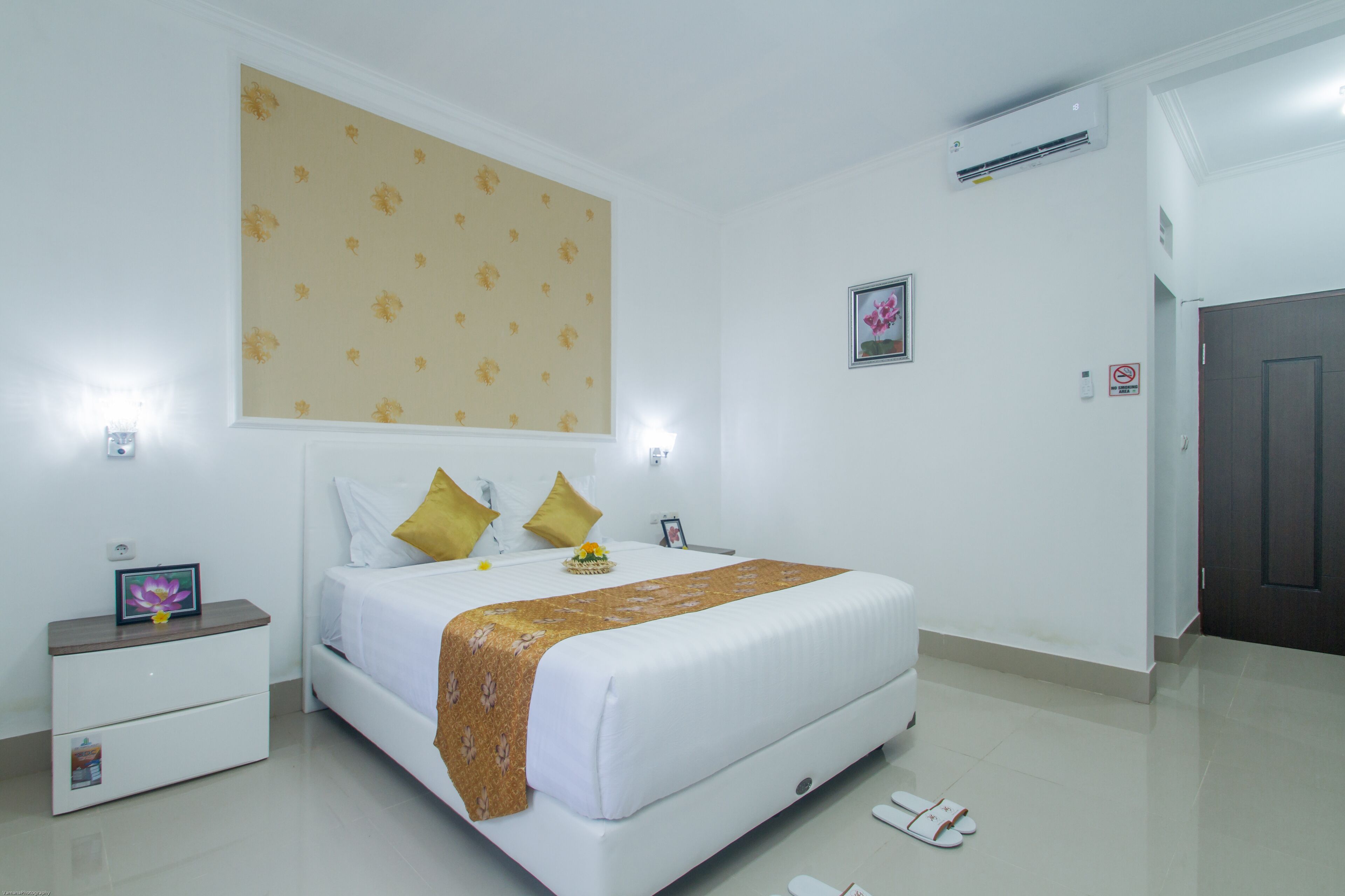 A hotel room with a large bed, a nightstand, a dresser, a wall-mounted air conditioner, and a door.