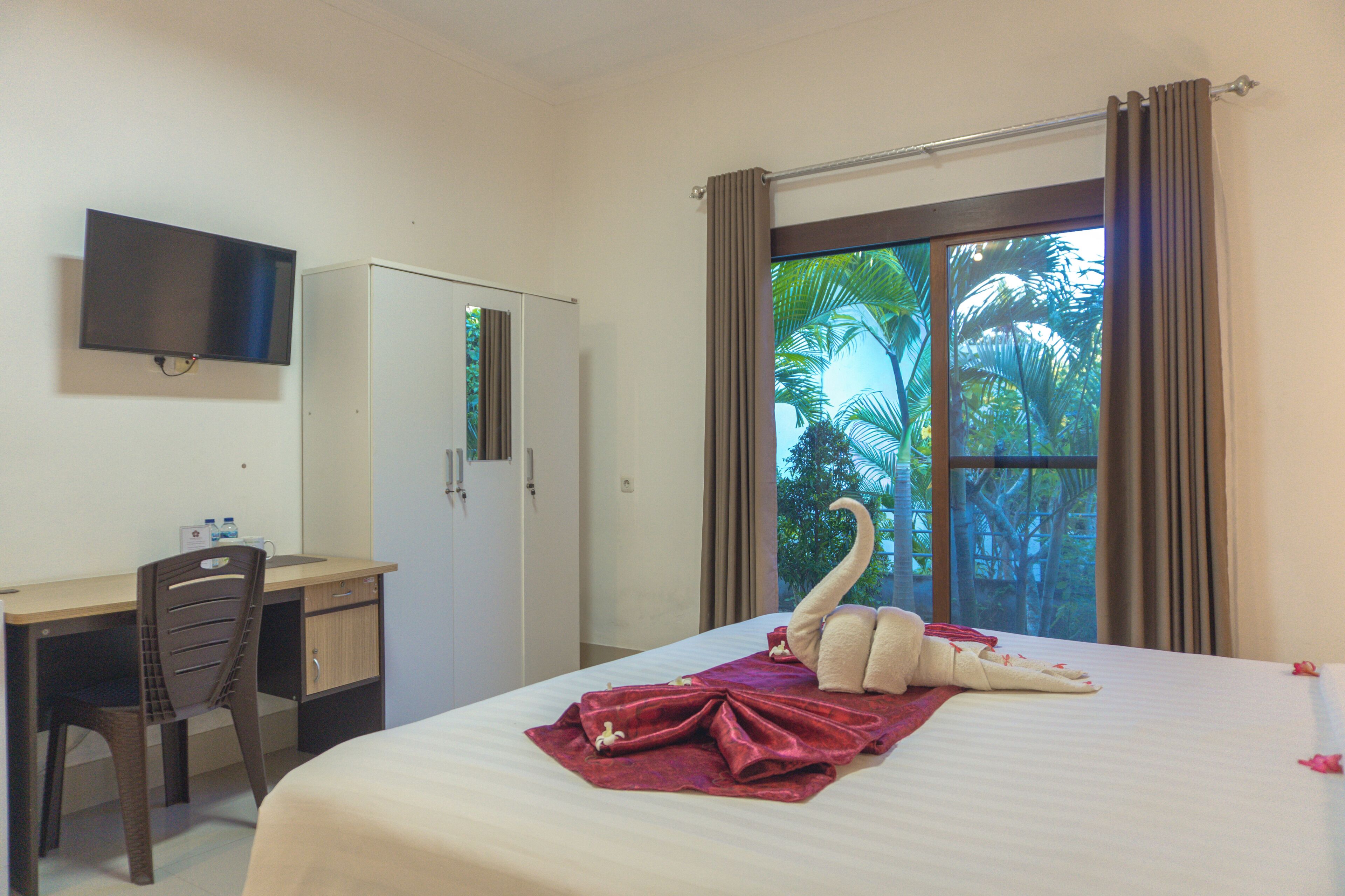 A hotel room with a bed, a desk, a chair, a TV, and a window with curtains.