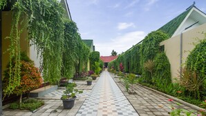 A pathway lined with potted plants and greenery, leading to a building with a red roof. - Kesari Penida by Mahaprana Home (Penida Island)