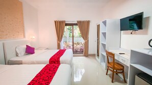 A hotel room with two beds, a desk, a chair, a TV, and a view of a garden through a glass door. - Kesari Penida by Mahaprana Home (Penida Island)