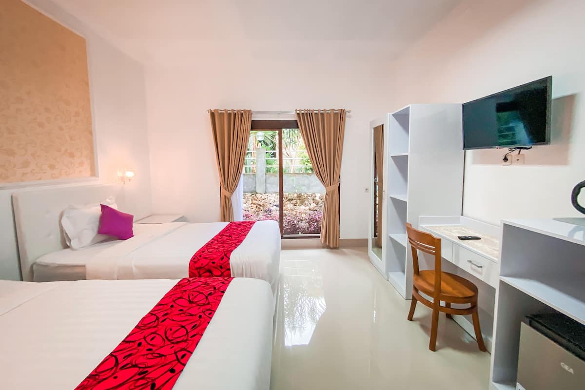 A hotel room with two beds, a desk, a chair, a TV, and a view of a garden through a glass door.