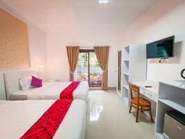 Habitación de hotel con dos camas, un escritorio, una silla, un televisor y vistas a un jardín a través de una puerta de vidrio.
