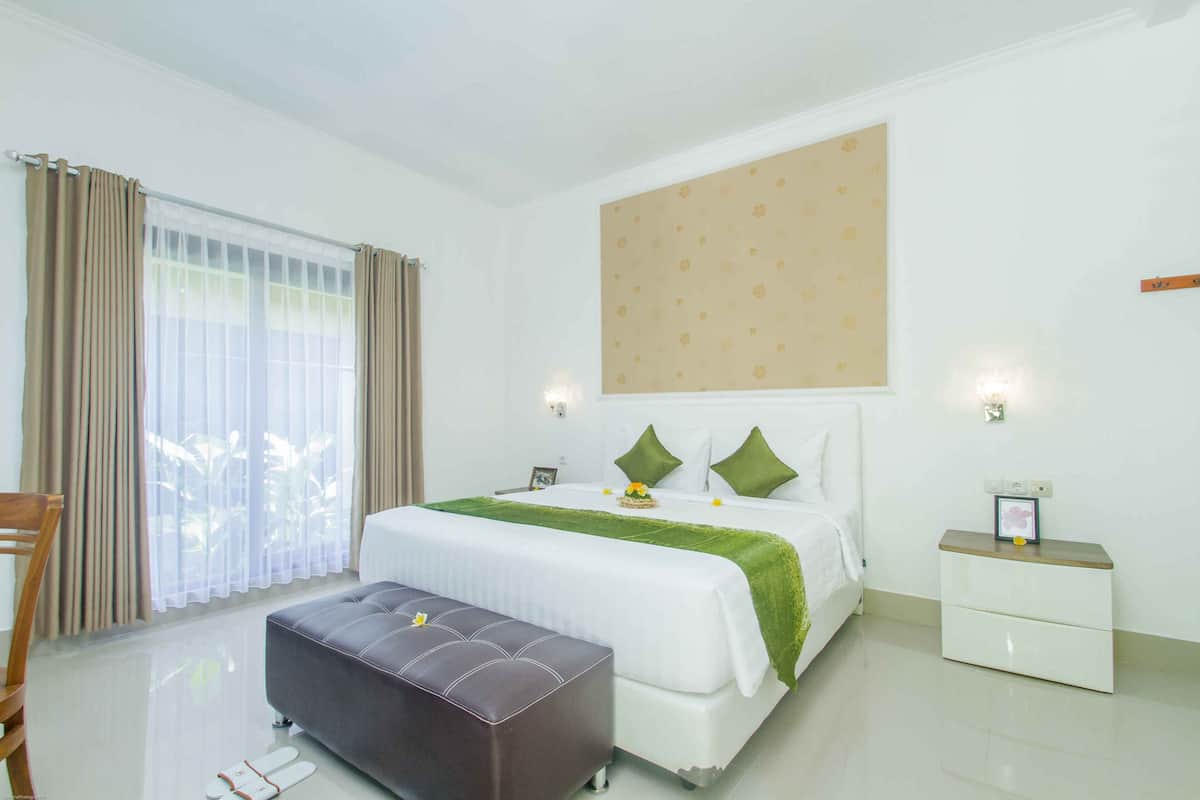 A hotel room with a bed, a bench, a nightstand, and a window with curtains.