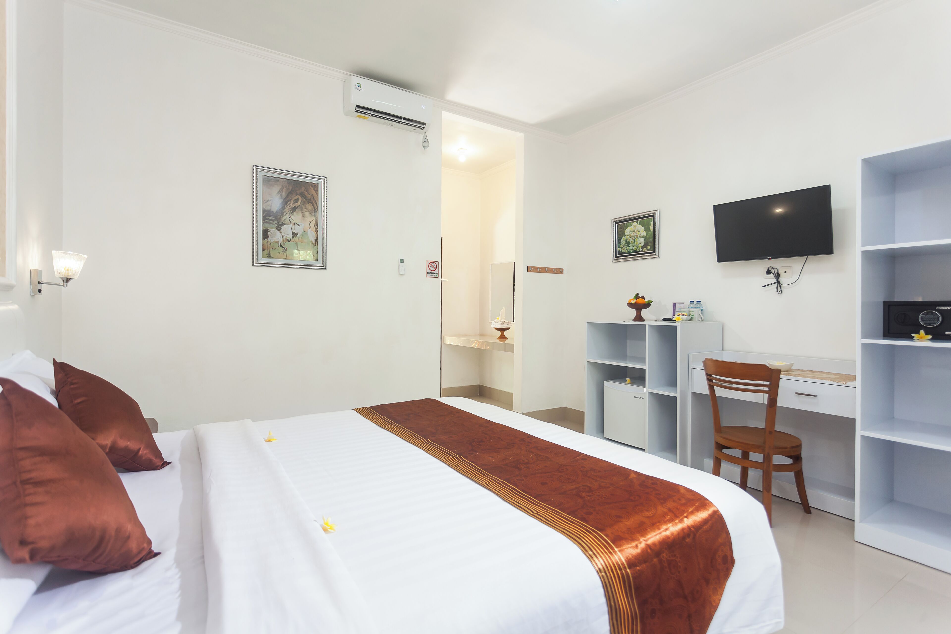 Habitación de hotel con cama, escritorio, silla, televisor y baño visible a través de una puerta abierta.