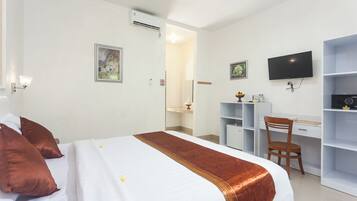 Habitación de hotel con cama, escritorio, silla, televisor y baño visible a través de una puerta abierta.