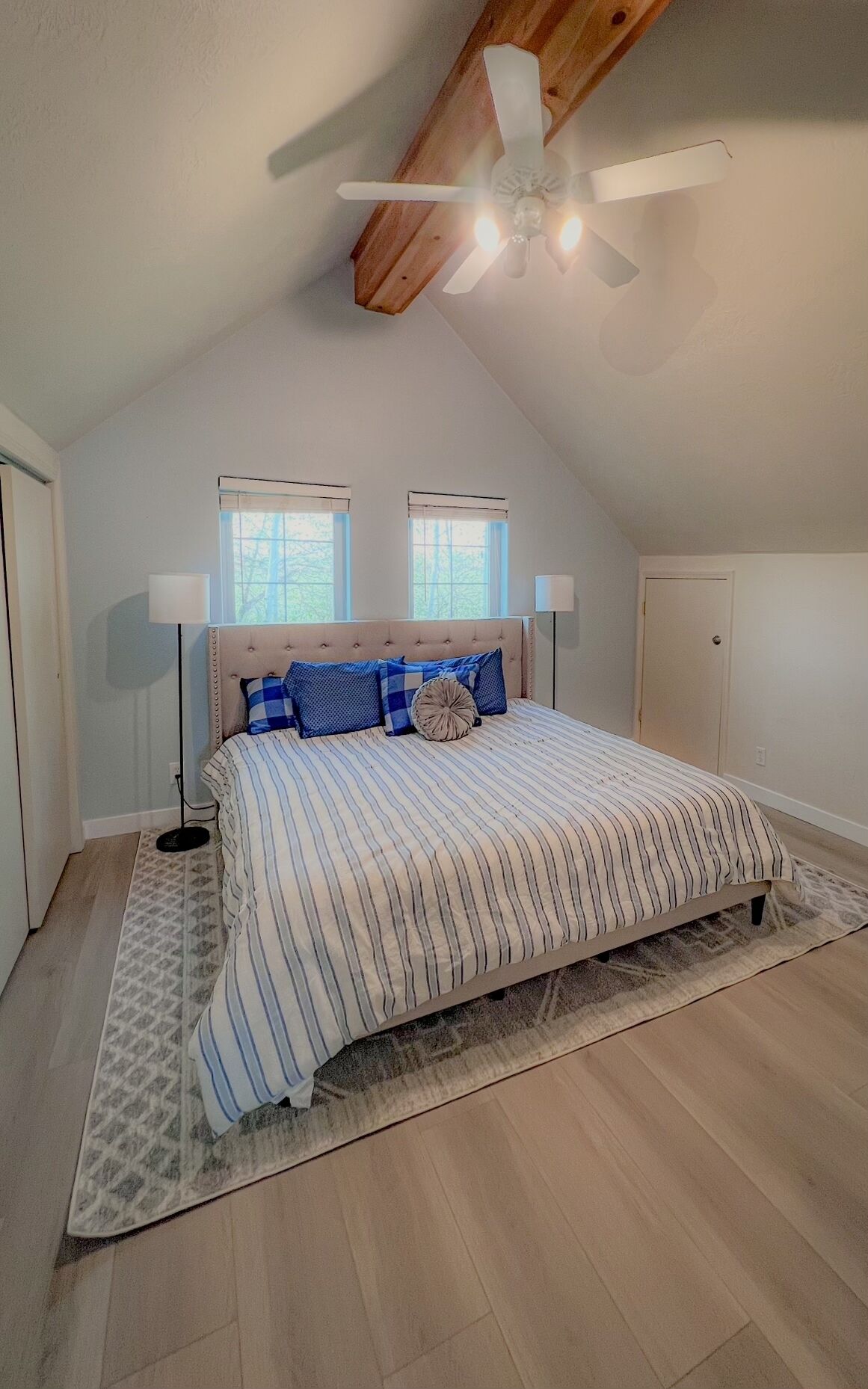 Une chambre à coucher avec un lit, deux fenêtres, un ventilateur de plafond et une porte.