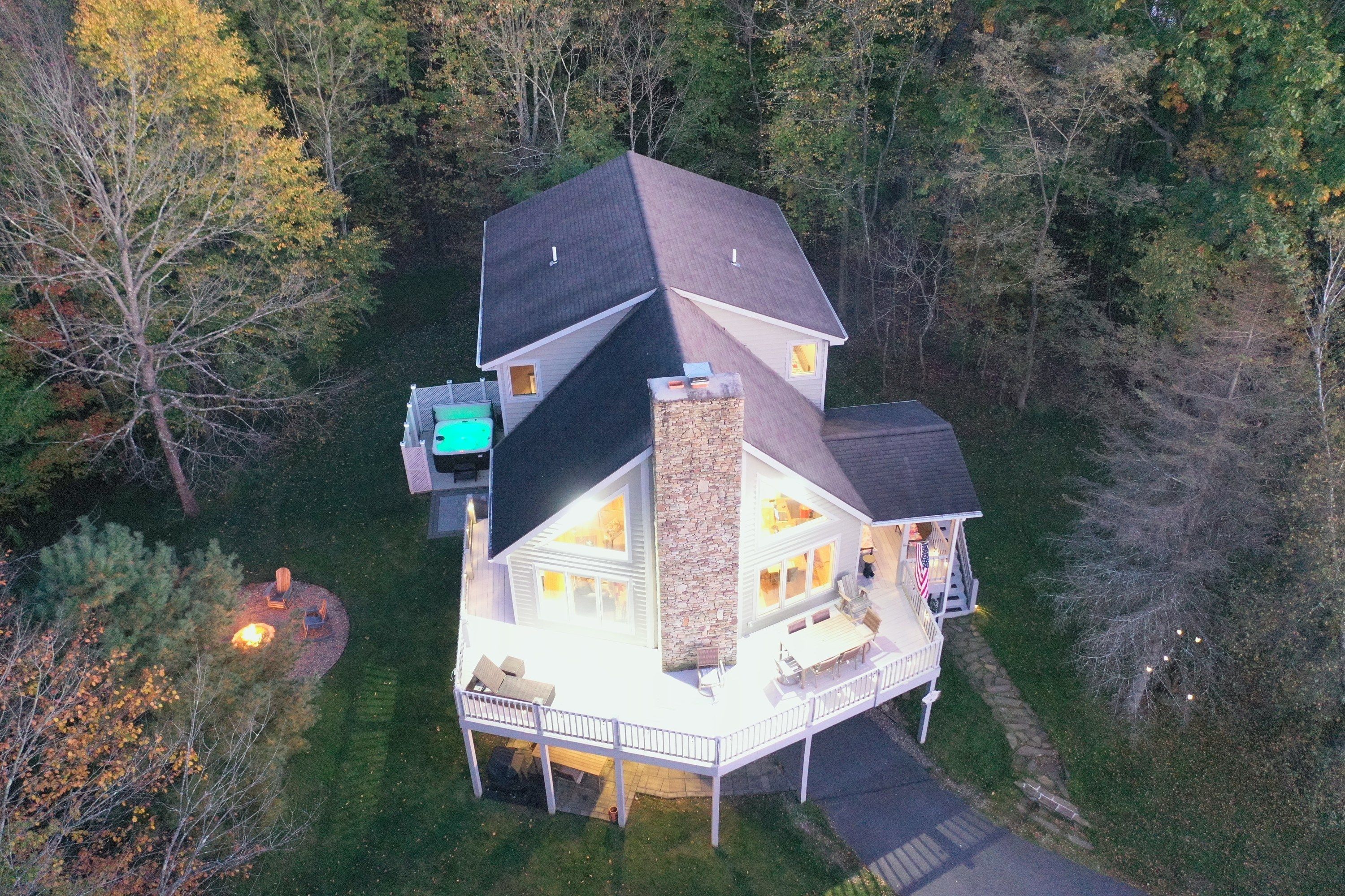 A two-story house with a stone chimney, a deck, and a small outdoor seating area.