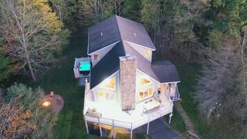 A two-story house with a stone chimney, a deck, and a small outdoor seating area.