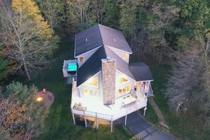 A two-story house with a stone chimney, a deck, and a small outdoor seating area.