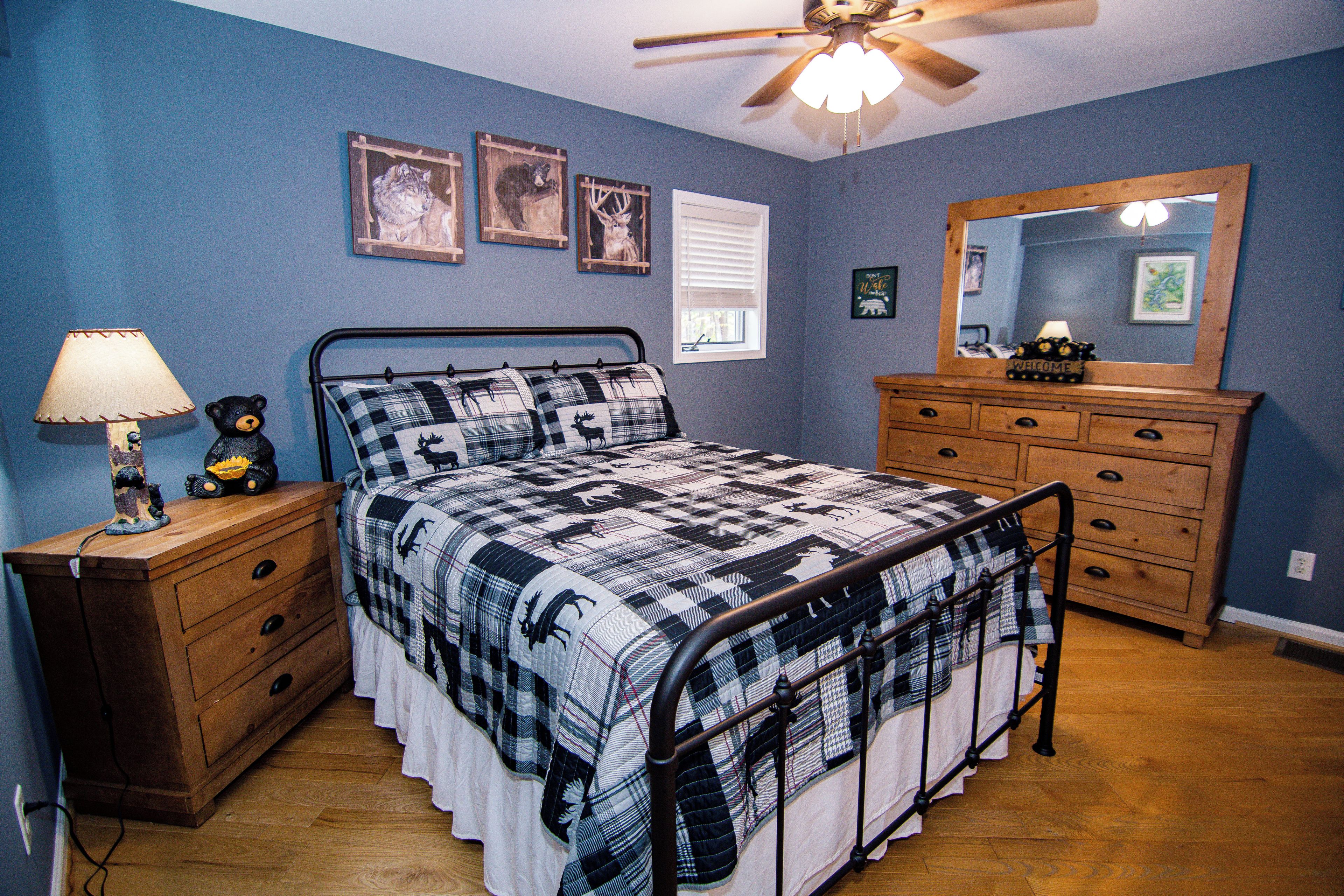 Een slaapkamer met een bed, een dressoir, nachtkastje, lamp en plafondventilator.