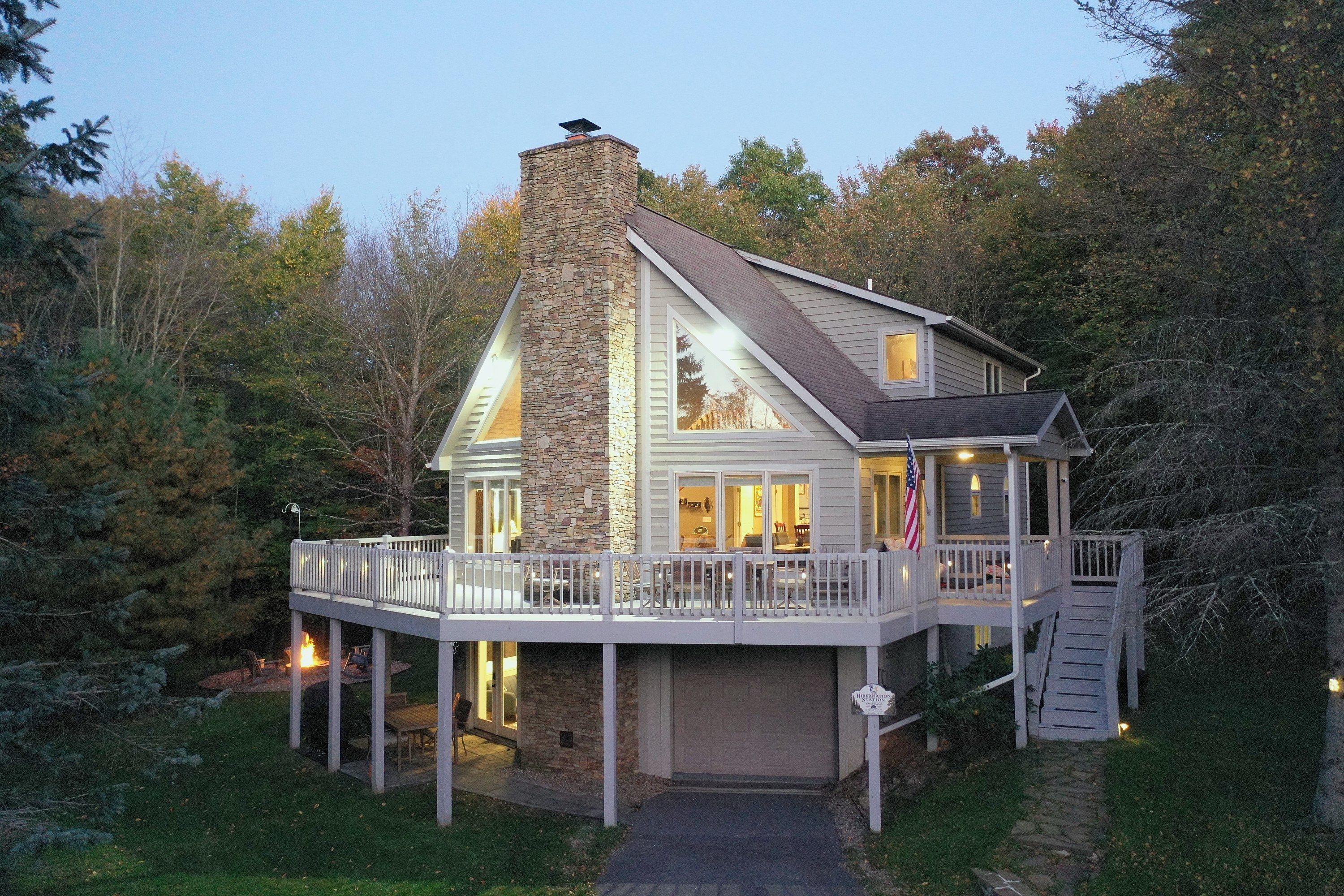 Hibernation Station at twilight: stone chimney, big deck, hot tub, fire pit and game room at Deep Creek Lake