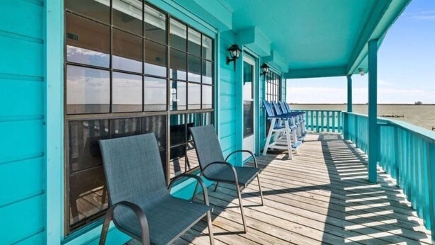 Um deck de madeira turquesa com duas cadeiras e guarda-corpo, com vista para a praia.
