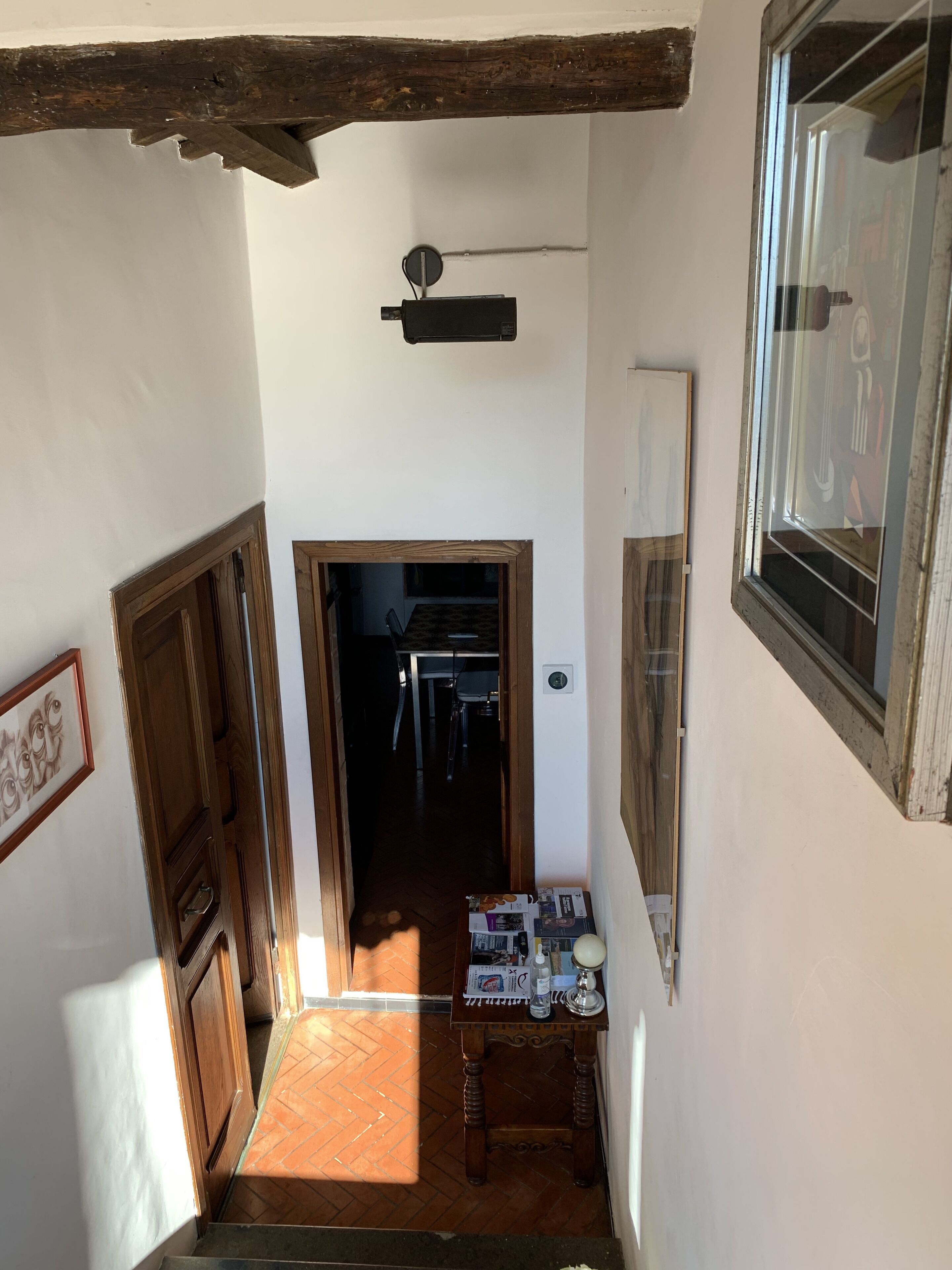 A narrow stairway leading to a room with a wooden ceiling, a window, and a door.