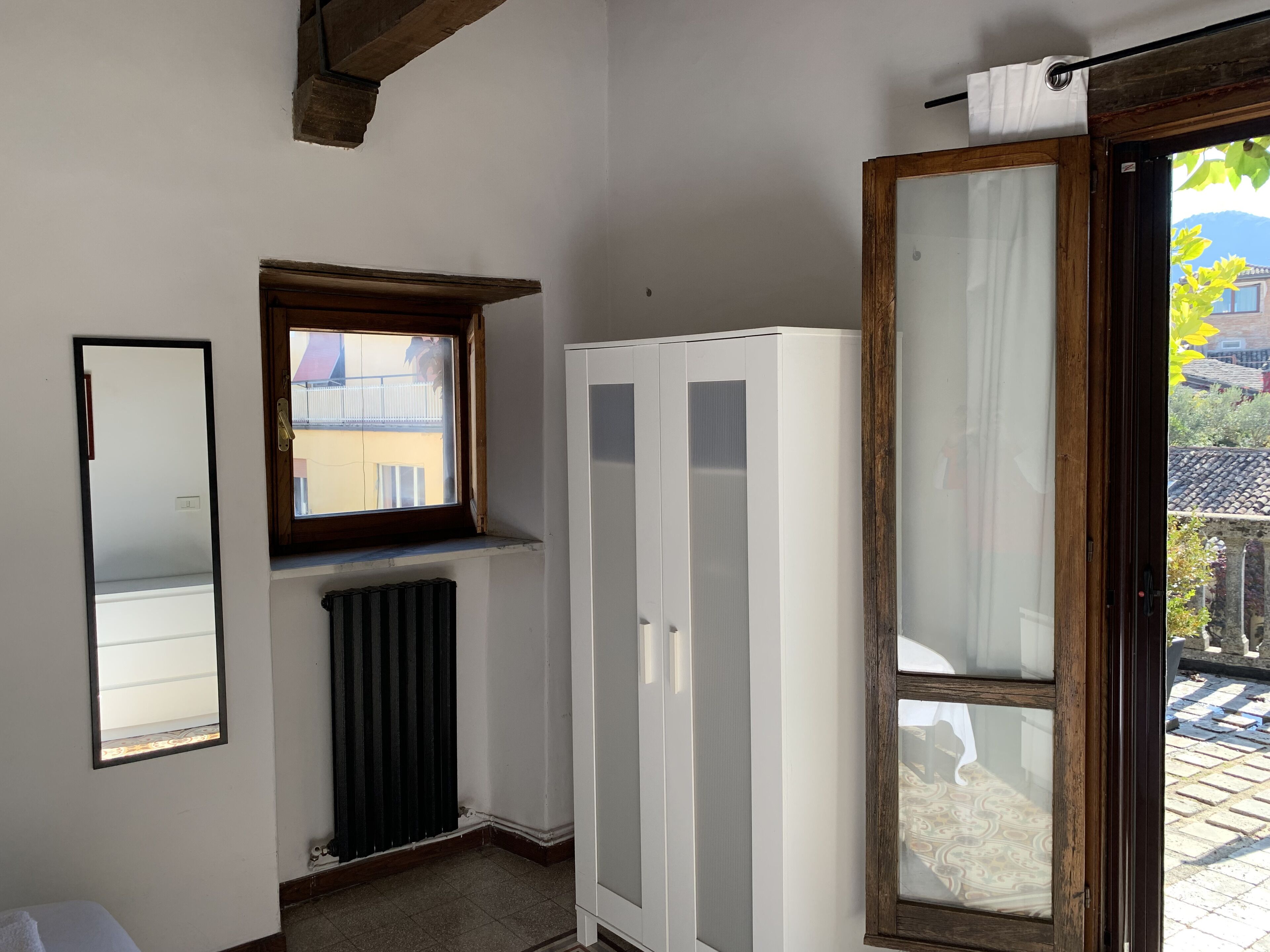 A small room with a window, a radiator, a wardrobe, and a door leading outside.