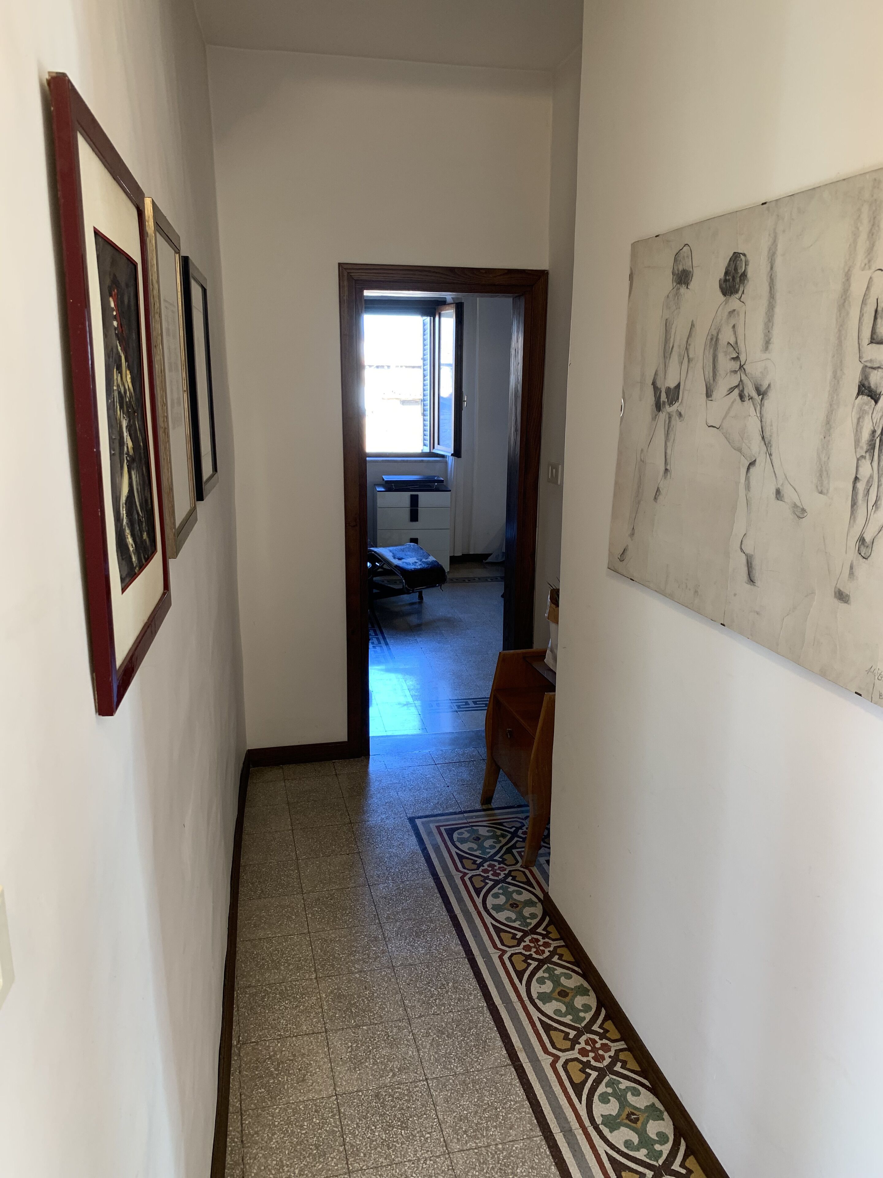 Un pasillo con alfombra estampada, un banco de madera y un cuadro en la pared.