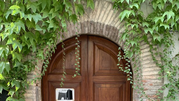 A wooden double door with a sign above it, set within a brick archway. - Porta Conca (Rieti)