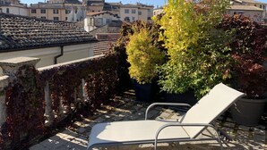 A rooftop terrace with a white lounge chair, potted plants, and a view of traditional buildings. - Porta Conca (Rieti)