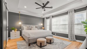 A modern bedroom with a bed, bedside tables, a ceiling fan, and a large window with curtains. - NEW - High End Luxury Home in the Heart of Atlanta (Atlanta)