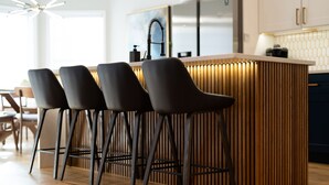A modern kitchen with a central island, black bar stools, and wooden flooring. - NEW - High End Luxury Home in the Heart of Atlanta (Atlanta)