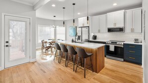 A modern kitchen with a central island, bar stools, a dining area with chairs, and a view through a glass door. - NEW - High End Luxury Home in the Heart of Atlanta (Atlanta)