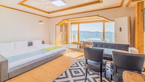 Habitación de hotel moderna con cama, sofá, zona de comedor y ventanas amplias con vistas a las montañas.