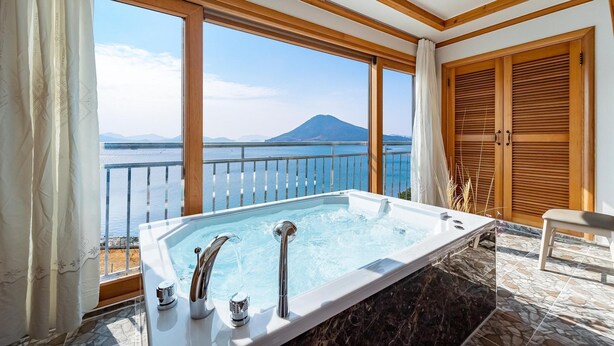 Un área de spa con bañera de hidromasaje, ventanas amplias y vistas al mar y las montañas.