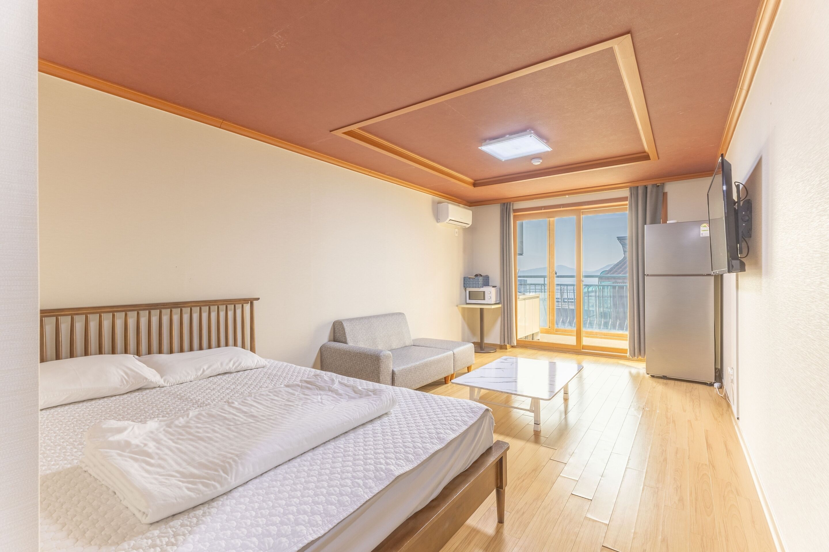 Un dormitorio con cama, sofá, televisor y ventana corredera a un balcón.