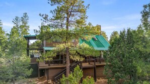 A cabin with a green roof, wooden deck, and a staircase leading to a balcony. - 4 Bedrooms, Sleeps 16, Hot Tub, Games, Tesla Charger, Smart TV's,  MORE! (Heber)