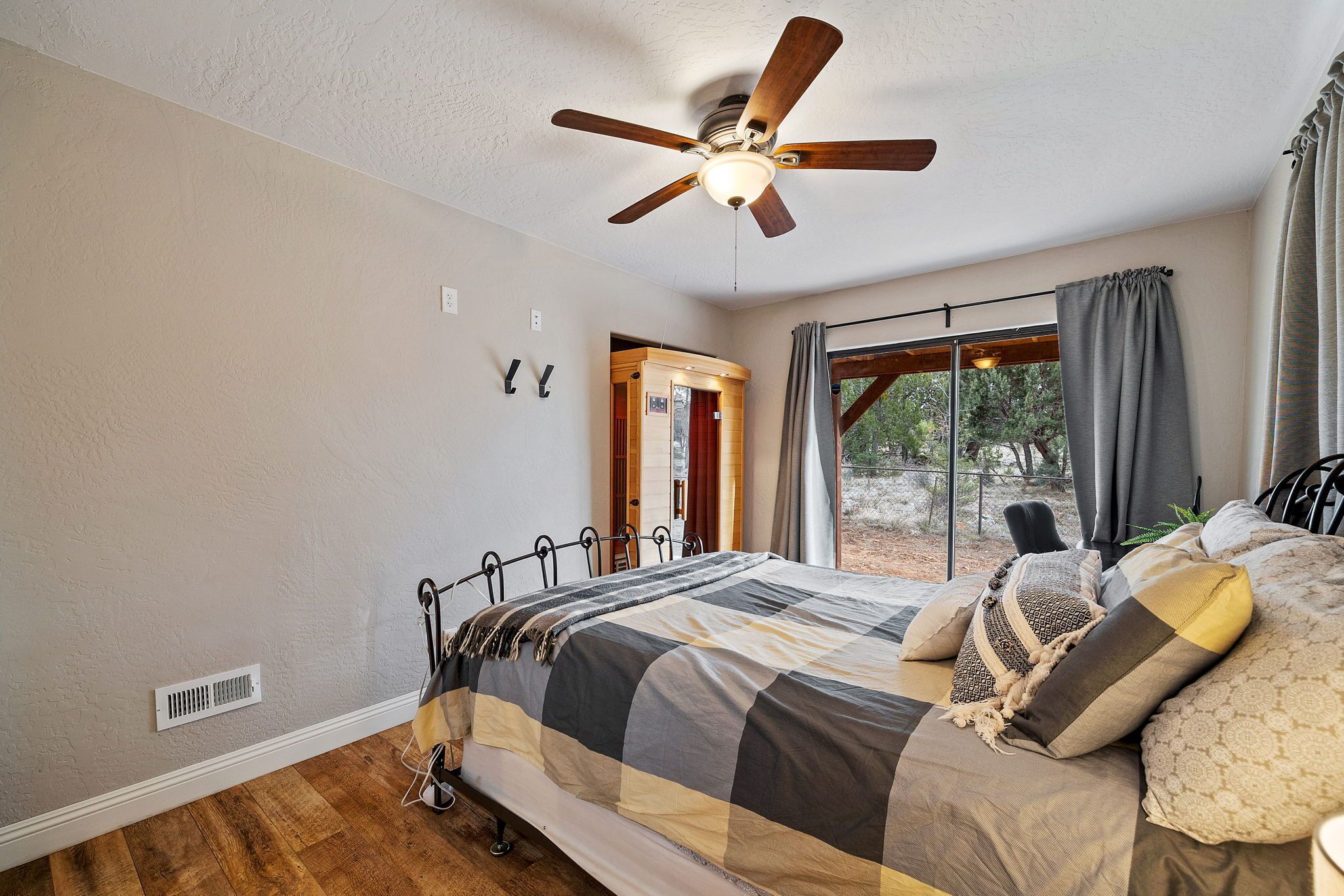 A bedroom with a bed, a ceiling fan, a window with curtains, and a door leading outside.