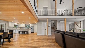 A spacious open-plan living area with a wooden floor, a dining table with chairs, a sofa, and a staircase leading to an upper level. - 4 Bedrooms, Sleeps 16, Hot Tub, Games, Tesla Charger, Smart TV's,  MORE! (Heber)