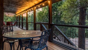 A covered outdoor area with a round table and chairs, surrounded by a wooden deck and railing, overlooking a forested area. - 4 Bedrooms, Sleeps 16, Hot Tub, Games, Tesla Charger, Smart TV's,  MORE! (Heber)