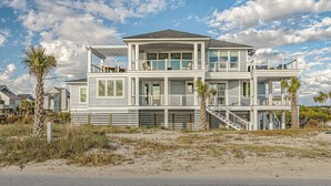 Ein zweistöckiges Strandhaus mit Balkon, großen Fenstern und einer Treppe, die zum Obergeschoss führt.