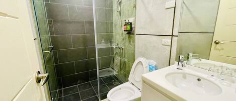 A bathroom with a glass shower enclosure, a toilet, and a sink.
